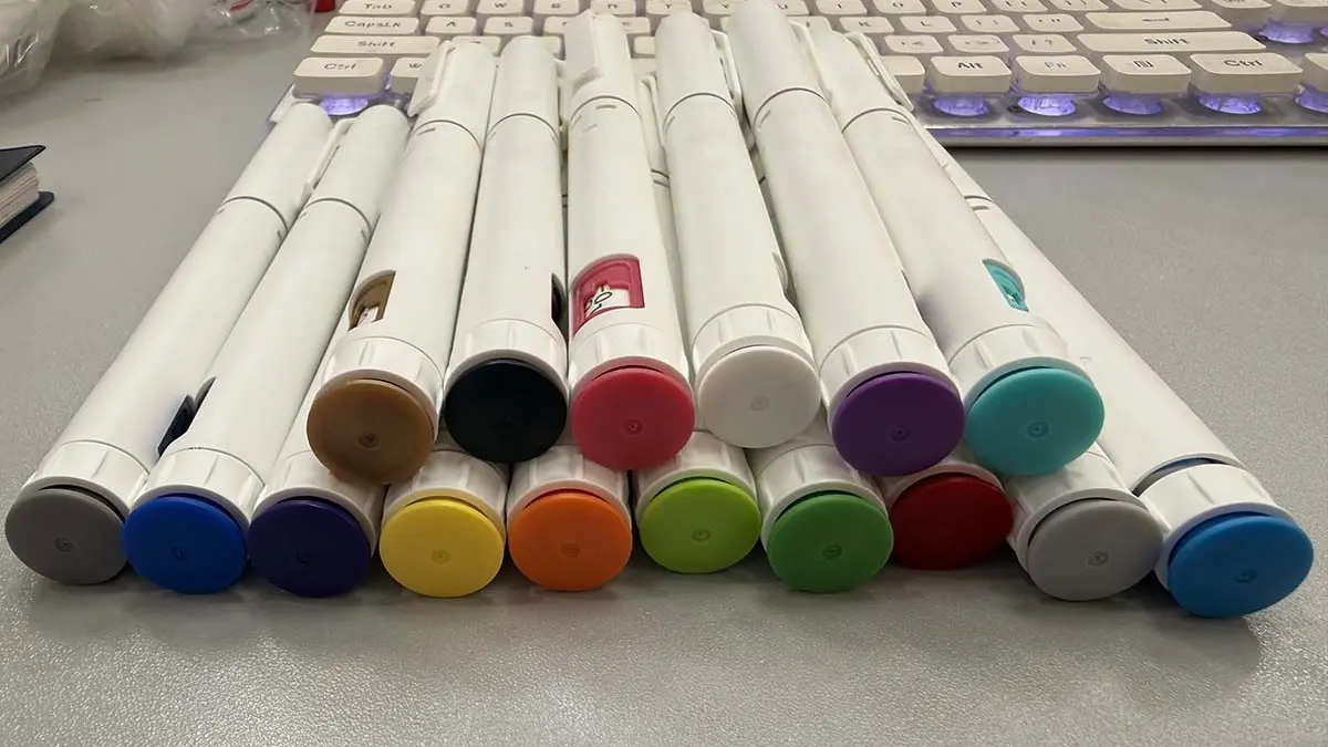WS-DS02 disposable injection pen color options — a dozen colored end caps including grey, black, tan, blue, navy, teal, green, yellow, orange, red and purple, lined up on a workbench